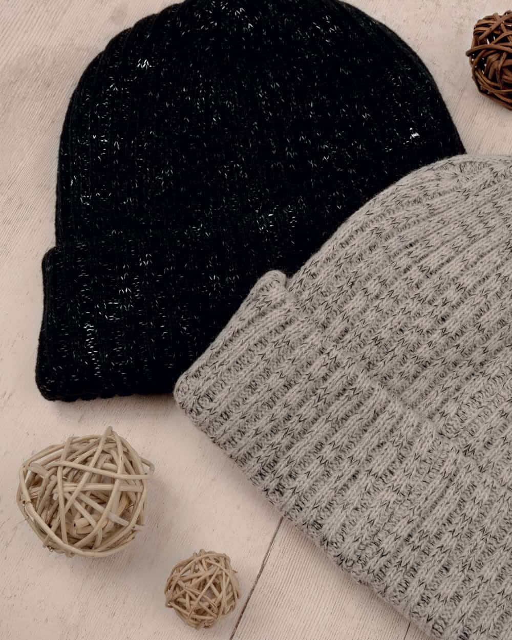 Two ribbed knitted caps, one black and one flecked grey, on a pale wooden surface
