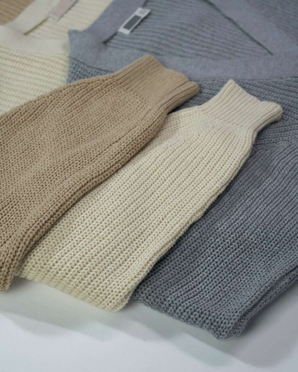 Cardigans folded and laid out in cream, oatmeal and grey, the rib and buttons visible