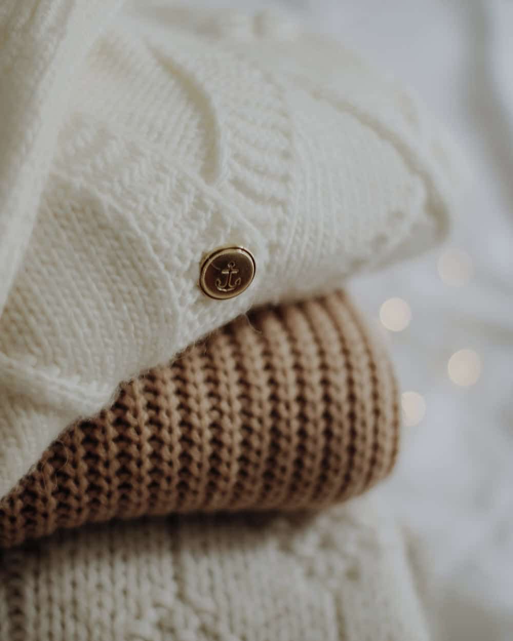 Folded pullovers stacked in cream and tan, cable knit with a metal button