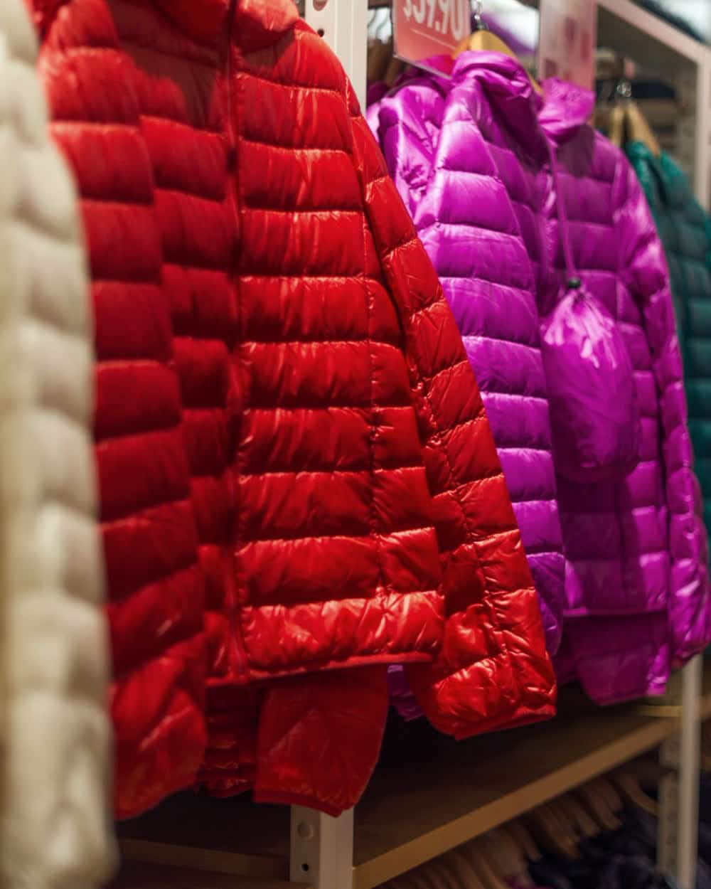 Quilted women's jackets in red on a rail beside an embroidered cream top