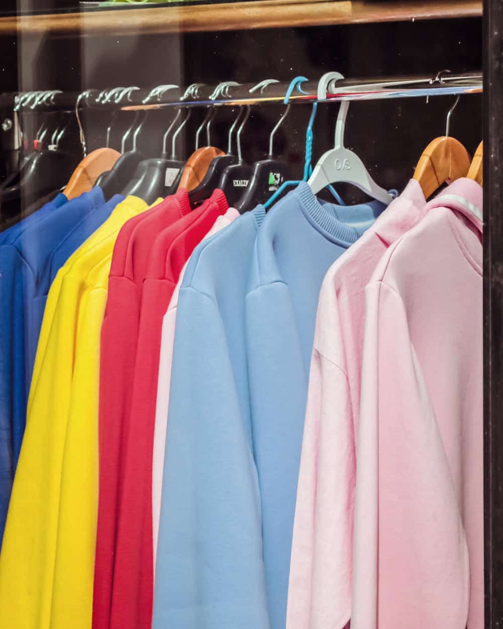 Sweatshirts on hangers along a rail in blue, yellow, red, pink and pale blue