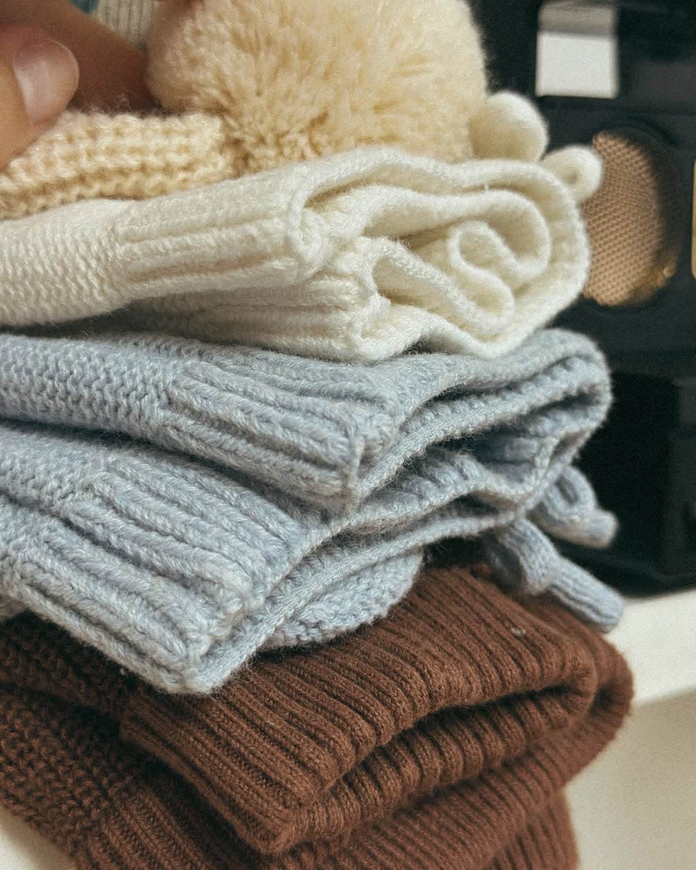 A stack of folded knitwear in beige, blue and brown, the knit picked out by side light