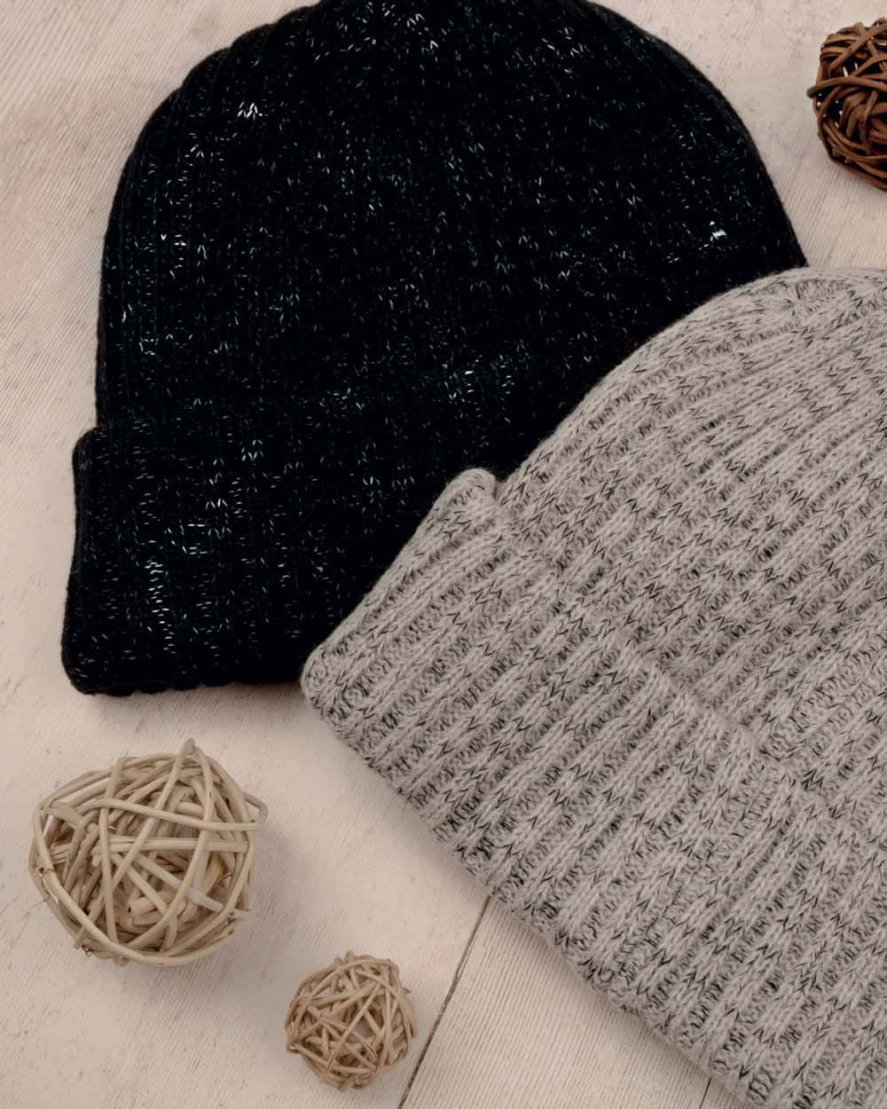 Two ribbed knitted caps, one black and one flecked grey, on a pale wooden surface