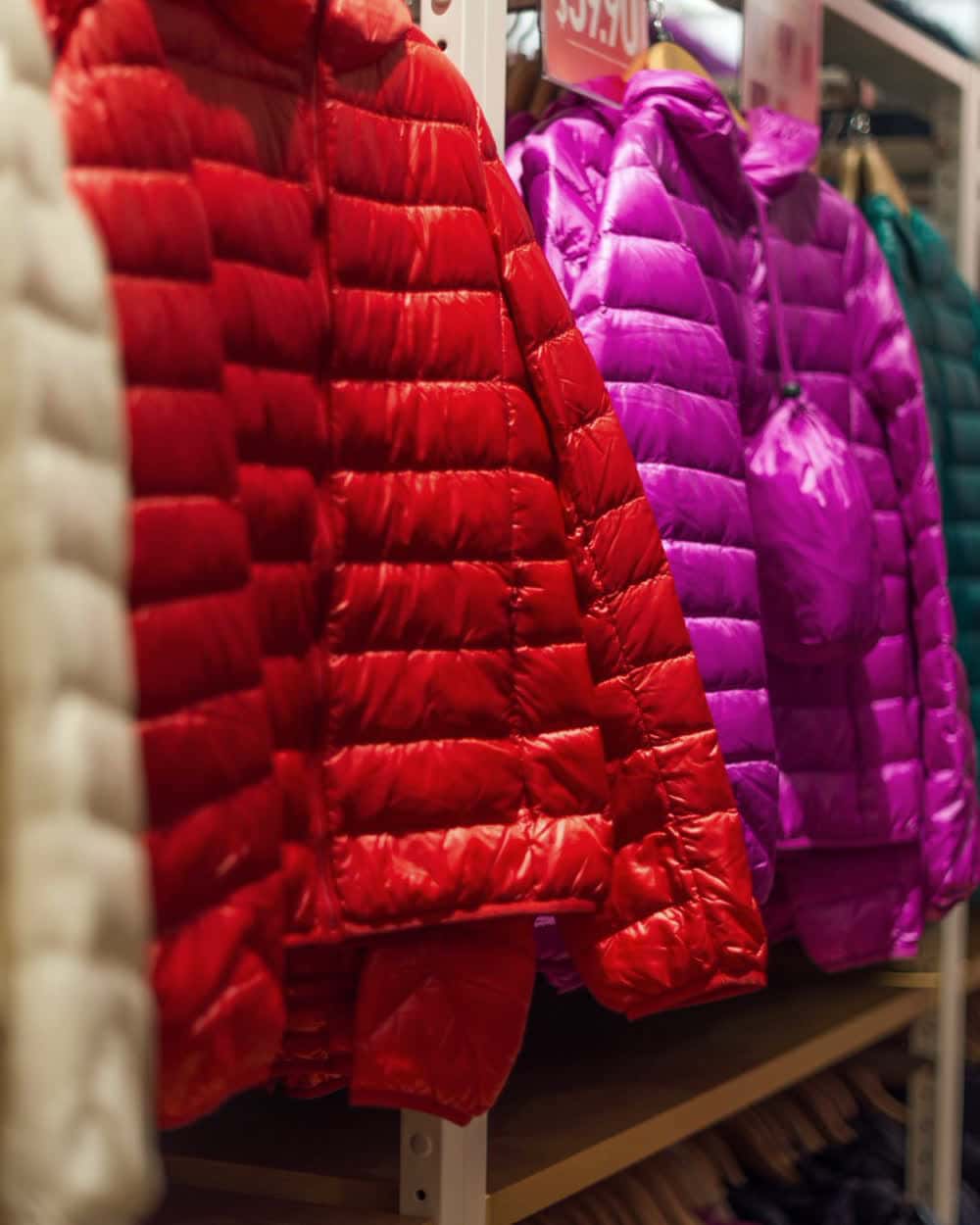 Quilted women's jackets in red on a rail beside an embroidered cream top